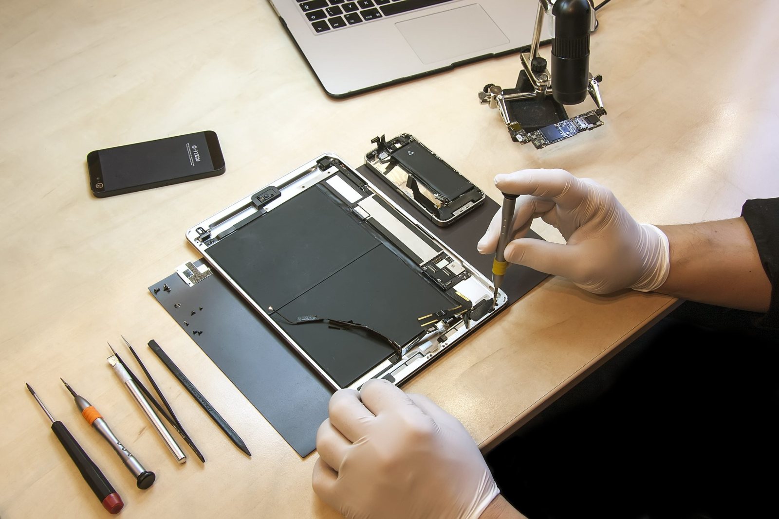 Technician in protective gloves repairing disassembled tablet device at workbench with tools