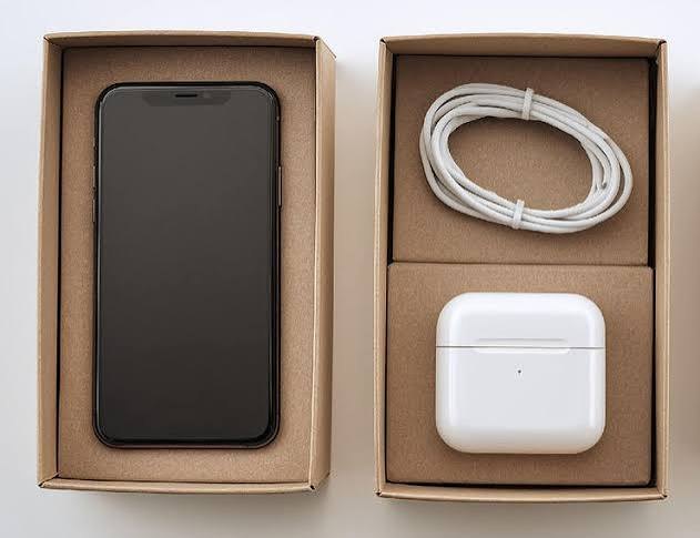 Unboxed smartphone with white charging cable and wireless earbuds case