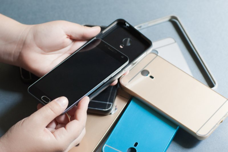 Person holding black smartphone with multiple phones displayed on gray surface