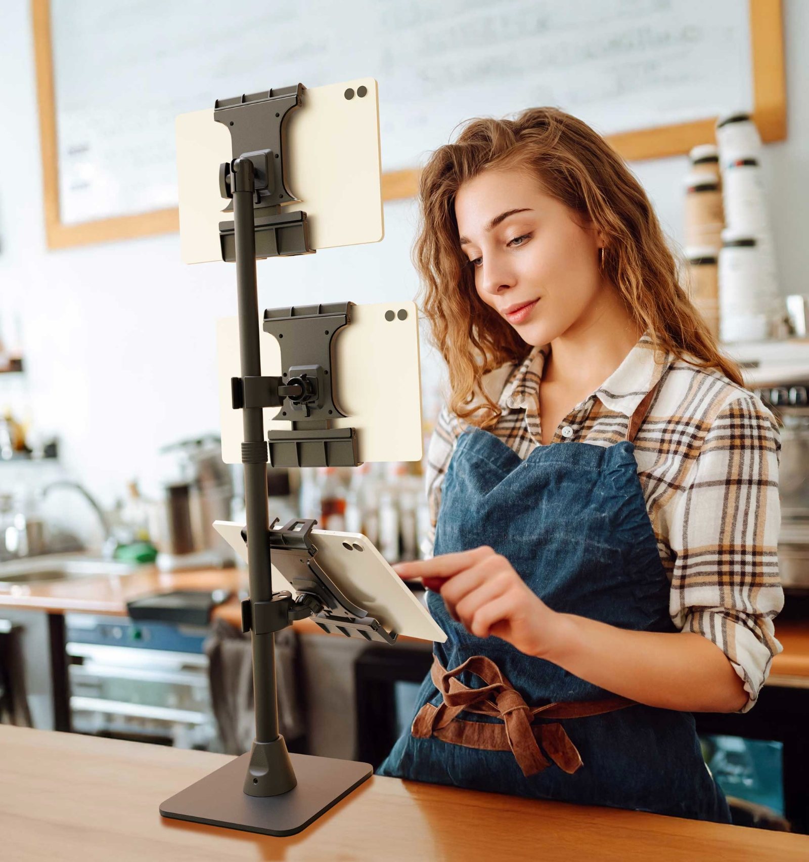 Woman in apron operating multi-device stand with tablets in workshop