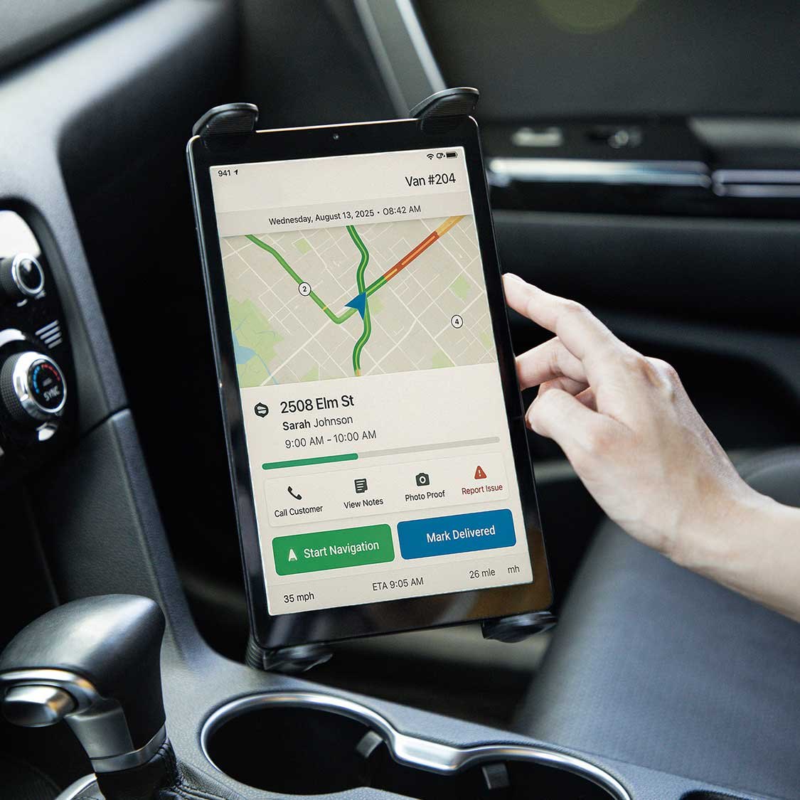 Delivery driver holding smartphone mounted in car showing route map, customer address, and navigation details for Van #204